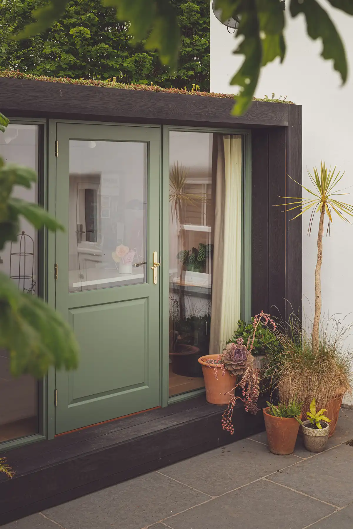a garden room with a green door, glass panel window, sedum living roof and a collection of plant pots