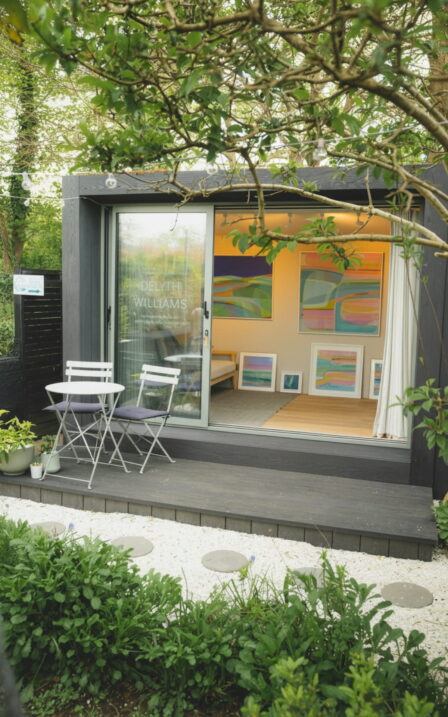 Exterior image of Delyth's Little Green Room with the doors open and lights on.