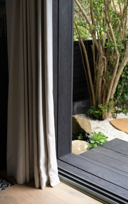 Curtains in Delyth's Little Green Room with the door open and decking in black millboard.