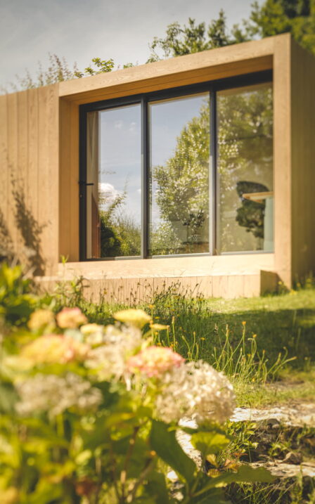 Flowers in the garden with Little Green Room in golden oak.
