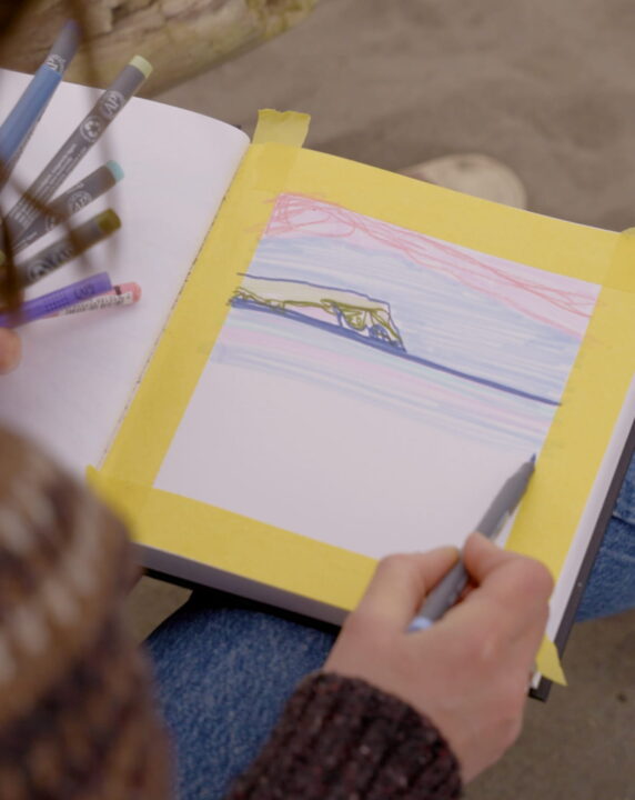 Close image of Delyth drawing on the beach.