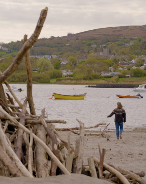 Delyth walking across the beach with boats on the water.